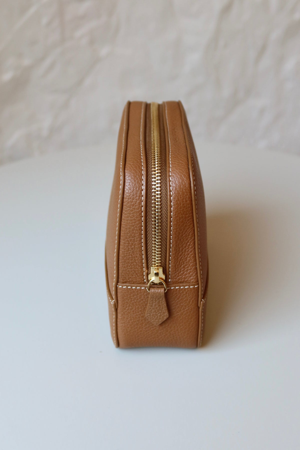 Soline Atelier EVERYDAY beauty case in camel leather with white stitching, gold logo and gold hardware, side view including zipper on a white background