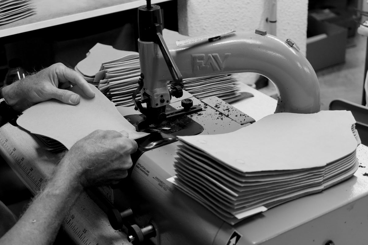 Black and white close-up of artisan hands cutting premium leather with a traditional cutting machine in a leather workshop